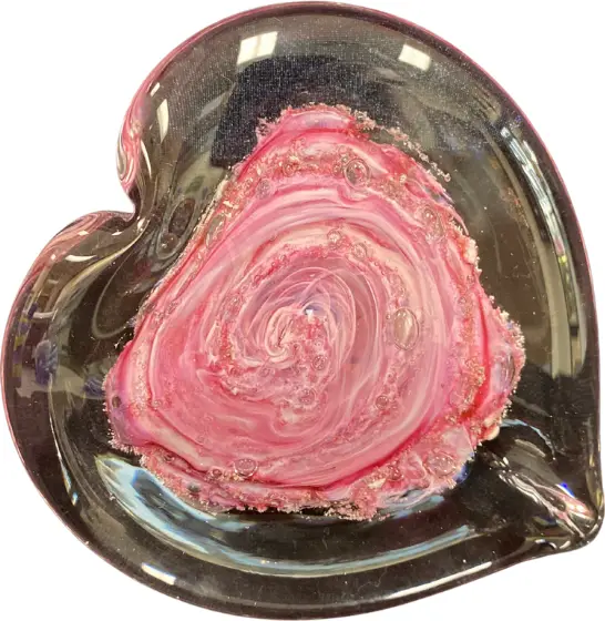 A clear glass heart with a swirl of pink glass and ashes at its center