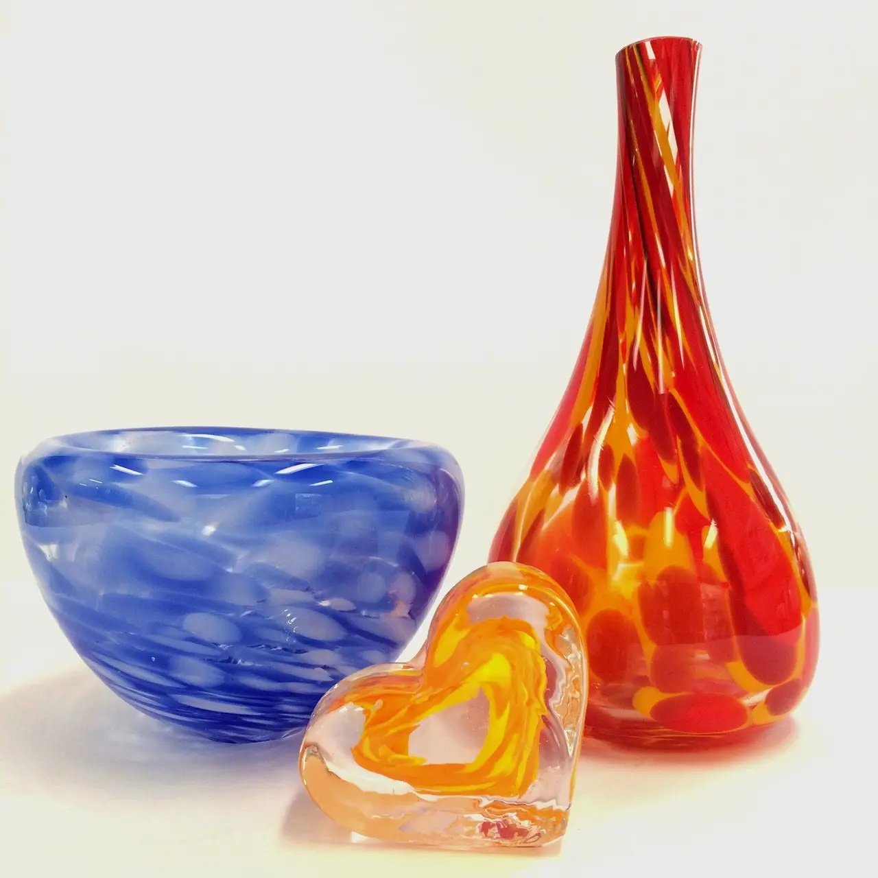 A speckled blue bowl, a tall orange vase and a small amber heart