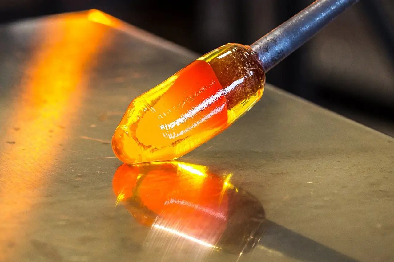 A glowing gather of molten glass on the end of a blowpipe, resting on a steel table